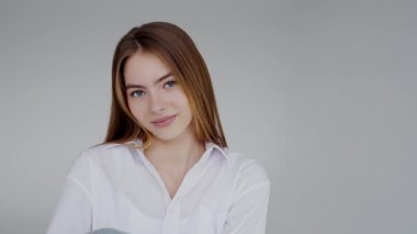 Sıradan beyaz gömlek giymiş kendine güvenen genç bir kadının portresi. Nazik bir gülüşü var. Tarafsız bir arkaplanda sakin ve profesyonel bir atmosfer yayıyor..