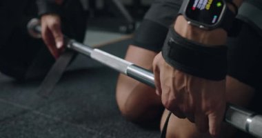 Spor salonunda halteri tutan bir adamın elleri, halter kaldırma sırasında akıllı saat verilerine odaklanıyor. Smartwatch ile Sıkı Beden Eğitimi Oturumunda Formda Adam