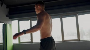 Odaklanmış genç bir adam güneşli bir spor salonunda esneyerek spor seansına hazırlanıyor. Sağlık ve etkinlik üzerinde duruluyor. Genç Sporcu Parlak Spor Salonunda Çalışmadan Önce Esneme