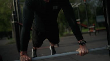 Açık hava spor salonunda şınav çeken odaklanmış bir sporcu. Doğal ortamdaki fitness ve adanmışlığı vurguluyor. Açık hava fitness parkında şınav çeken genç adam.