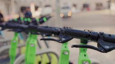 Parlak yeşil bisiklet sıraları düzgün park edilmiş ve hareketli bir şehir caddesinde kullanılmaya hazır, bulanık arka plan şehir hareketini ve trafiğini kaydediyor. Yoğun bir caddede Yeşil Kiralık Bisikletler Sıralanmış