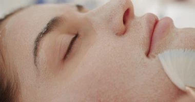 Müşteri için bir güzellik salonunda profesyonel prosedür. Yüz yenileme konsepti. Genç kadın kozmetik ilaç tedavisi görüyor, yakın plan. Güzellik uzmanı fırçayla kadın yüzüne köpük maske yayar