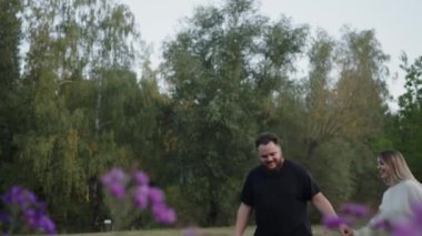 Canlı çiçekler ve yeşilliklerle çevrili yemyeşil bir çayırda gezen neşeli bir çifti yakalayan hoş bir görüntü. Aşk, ilişkiler ve doğa temaları için mükemmel..