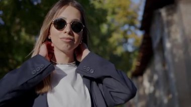 Uzun sarı saçlı, güneş gözlüğü takan, şehir ortamında güneşli bir günün tadını çıkaran şık bir genç kadının yakın çekimi. Kendine güvenen, rahat bir hava yayıyor. Şehirde Güneş Gözlüklü Genç Kadın