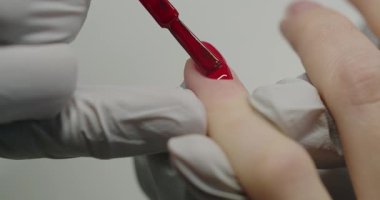 Manikürcü müşteri tırnaklarını parlak kırmızı ojeyle boyuyor. Manikür ustası eldivenler içinde müşterilerinin tırnaklarına kırmızı jel sürerek güzellik salonunu boyuyor. Kadın elleri için profesyonel bakım. Güzellik salonu.