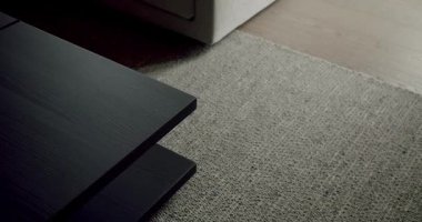 Sade siyah bir sehpanın dokulu gri bir halıya karşı durduğu şık bir evin yakın çekim görüntüsü. Kalıplı Siyah Masa ve Gri Halı ile Zarif İç Tasarım