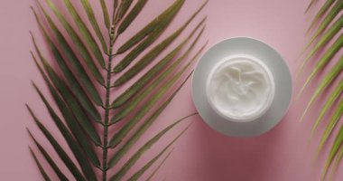 Palmiye yapraklı beyaz şişe stüdyoda pembe arka planda kozmetik için dönüyor. Doğal malzemelere, vücut bakımına ve cilt bakımına dayalı kozmetik yağı, güzellik tedavisi için kavanoz kremi,