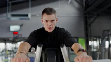 Modern Spor Salonunda Bir Makine Üzerinde Çalışan Genç Adam. Odaklanmış genç bir adam spor yaparken spor yapıyor. Çağdaş bir spor salonunda spor yapıyor. Siyah bir kıyafeti var..