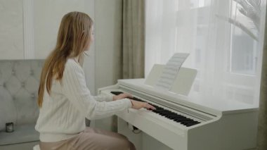Genç kız evde piyano çalışıyor. Eğitim ve öğrenim geliştirme konsepti. Odaklanmış genç, güzel bir kız. Elektrikli piyano çalarak eğleniyor. Müzik dersi veren genç bir müzisyen..