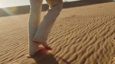 Çıplak ayaklı biri kum tepeciğinde yürür ve arkasında ayak izleri bırakır. Çölde gün batımında kumda yürümek. Doğayı keşfetmek, yalnızlığın ve huzurun tadını çıkarmak. Macera ve özgürlük kavramı.