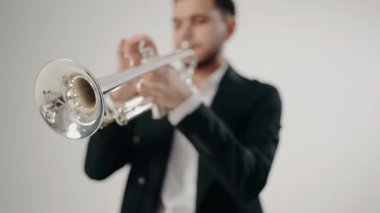 Takım elbiseli genç ve yakışıklı bir adam arzu ve ilhamla trompet çalar. Modern bir stüdyoda beyaz arka planda trompet çalan bir erkek caz şarkıcısı. Canlı caz konseri..
