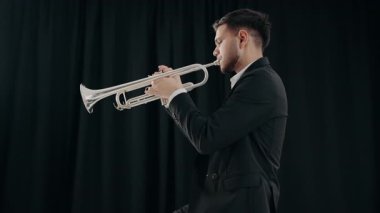 Takım elbiseli genç ve yakışıklı bir adam arzu ve ilhamla trompet çalar. Canlı caz konseri. Müzik tutkusu. Genç trompetçinin yakın eli. Müzik odası.