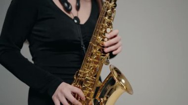 Siyah elbiseli genç bir kadın stüdyoda beyaz arka planda saksafon çalıyor. Siyah bir gece elbisesi giymiş, sahnede solo yapan bir kadın saksafoncu..