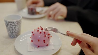 Zarif bir şekilde hazırlanmış pembe bir tatlıyı beyaz tabakta kırmızı parçalarla süsleyen ve yanında modern bir kafe ortamında şık bir kahve fincanı olan bir kişi. Gurme Pembe Tatlının Tadını Çıkarıyorum