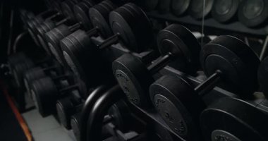 Profesyonel bir jimnastik salonundaki çeşitli halterlerin raflarına detaylı bir bakış. Güç antrenmanı ve zindelik atmosferini vurguluyor. Profesyonel Spor Salonu Ekipmanları Dolduruldu