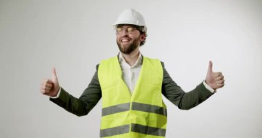 Sert şapka ve güvenlik yeleği giyen neşeli bir mühendis onay, memnuniyet ve olumlu geri bildirim veren iki başparmak kaldırıyor. Bu jest sanayide güven ve başarı taşır.