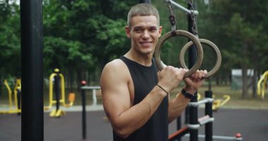 Yakışıklı sporcu jimnastik yüzükleriyle egzersiz yapmaya hazırlanıyor. Adam egzersiz yaparak kol kaslarını geliştiriyor. Spor yüzükleri üzerinde fitness egzersizi yapan formda bir adam. jimnastik yüzükleri.