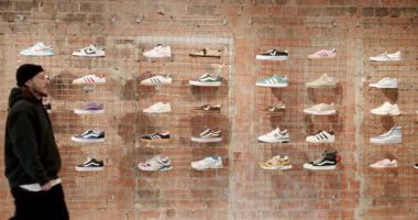 Genç bir adam bir pano dükkanında spor ayakkabı sergisinin önünden geçiyor. O, sergilenen çeşitli ayakkabılara bakıyor. Ayakkabılar renkli ve şık görünüyor. Chisinau, Moldova - 18 Ocak 2025