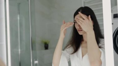 Banyodaki aynaya bakarken cilt bakımı yapan kadın. Kişisel bakım kavramı, günlük güzellik rutinini vurgulamak ve cilt bakımı sağlıklı, parlayan ciltler için. Cilt Ürünü Uygulayan Kadın