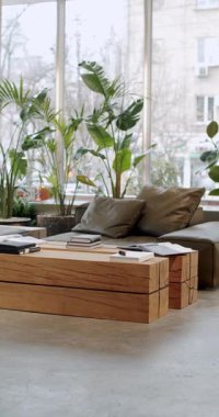 Rahat bir kanepesi, ahşap mobilyası ve yemyeşil bitkileri olan modern iç tasarım. Doğal ışık geniş pencerelerden akar, alanı aydınlatır ve hoş bir atmosfer yaratır..