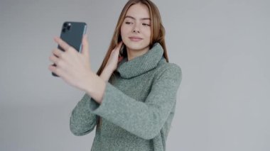 Akıllı telefonuyla selfie çeken, telefona odaklanmış ve elini uzatmış genç bir kadının bulanık görüntüsü. Yeşil Süveterli Genç Kadın Akıllı Telefonla Selfie Çekiyor
