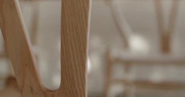 Hafif ahşap sandalyelerin yakın plan düz, kıvrımlı çerçeve, doğal ışıklandırılmış bir alanda benzer sandalyelerin yumuşak ve bulanık arka plan üzerine kurulur. Doku ve tasarıma odaklanmak bir sakinlik duygusunu davet eder..