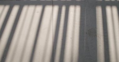 Döşeme üzerinde metal korkulukların gölgesi. Fayanslar üzerinde hareket eden gölgelerin soyut arkaplanı. Işık ve gölge deseni. Parmaklıkların arasından parlayan güneş ışığı çizgili bir gölge deseni yaratır..