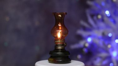Masanın üzerinde küçük bir gaz lambası duruyor. Arka planda bir Noel ağacı