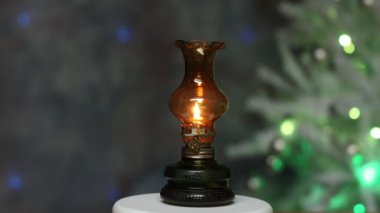 Masanın üzerinde küçük bir gaz lambası duruyor. Arka planda bir Noel ağacı