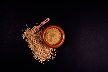 İçinde kişniş tozu olan Clay Pot 'un en iyi görüntüsü. Siyah kağıt yüzeyinde plastik kaşık olan kişniş tohumları. Siyah Kağıt Arkaplanda İzole Edilmiş. Boşluğu Kopyala