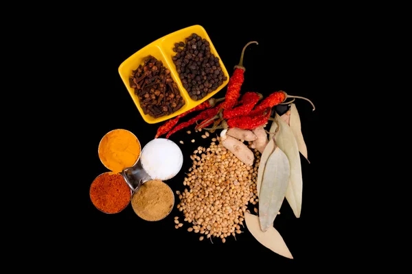 Round Bowls In Spices Like, Red Chili Powder, Turmeric Powder, Salt And Coriander Powder. One Double Box Square Bowl In Black Pepper And Clove. Isolated On Black Background. Dried Red Chilies, Coriander Seeds, Raw Turmeric And Cinnamon Leaves On Blac