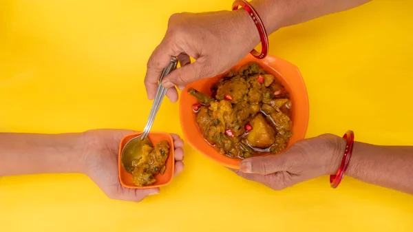 印度女性给另一个女孩一勺混合蔬菜Sabzi的头像 橙碗中混合蔬菜Gujarati Rasiya Muthia 黄色背景隔离 — 图库照片