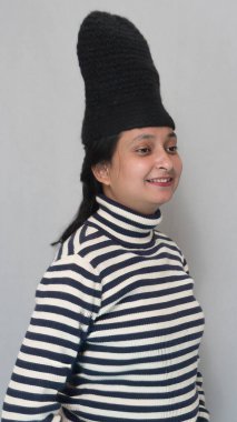 Genç bir Hintli kızın portre görüntüsü, balıkçı yaka kazak giyiyor siyah beyaz çizgili kazak, yünlü siyah şapkalı, kış sezonunda izole edilmiş beyaz arka plan.