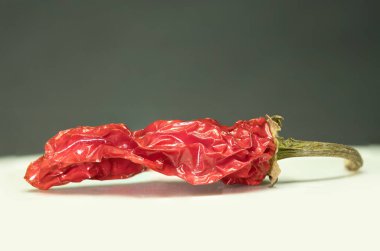 Spice of Life: A Close-Up of a Vibrant, Aged Red Chili Pepper, Bu resim tek bir kırmızı biberin yakın çekimini içeriyor. Buruşuk dokusu ve yoğun kırmızı rengi olgunluğu gösteriyor.