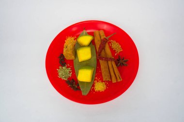 Kırmızı biber, karanfil, siyah kakule, anason tohumu ve diğerleri dahil olmak üzere mango turşusunda sıklıkla kullanılan Hint baharatlarının bir çeşidi, beyaz bir arkaplanda kırmızı bir tabakta tepeden tırnağa sunulmaktadır..