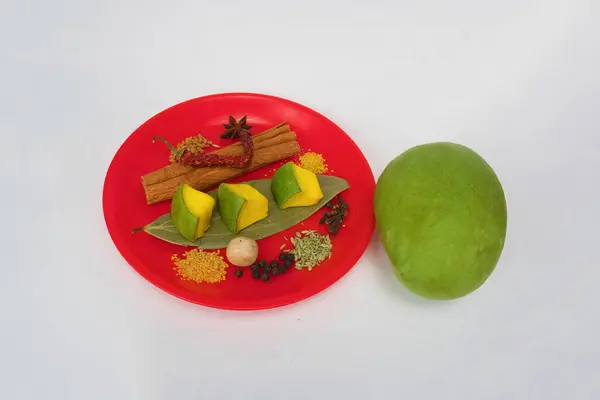 Stock image different type of spices on red dish and mango pieces with raw mango, isolated on white background