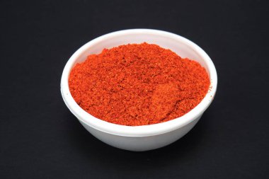 Kırmızı biber tozu beyaz kasede, siyah arka planda izole edilmiş.