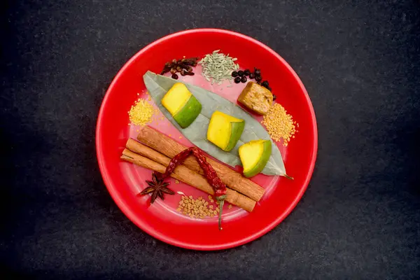 Stock image Mixed indian spices for mango pickle like, red chilli, black pepper, clove, black cardamom, anise seeds etc. in red plate, isolated on black background