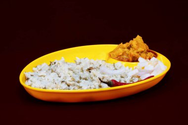 Khichdi ile Gujarati Kathiyawadi Baharatlı Dhokali Sabji 'nin sağdan görünüşü, belirgin bir şekilde sarı tabakta, siyah bir arkaplan üzerine kuruludur.