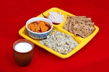 Gujarati Kathiyawadi Spicy Dhokali Sabji, khichdi, Roti, Onion Pieces, Red Chilli, on yellow square dish with a glass of butter milk on left side, copyspace on top and bottom, Top Cross view clipart