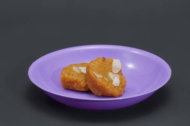 Two pieces of Mohanthal are presented on a small purple plate, showcasing this traditional Gujarati delicacy clipart