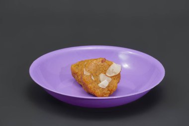 İki parça Mohanthal, küçük mor bir tabakta, geleneksel bir Gujarati tatlısı.