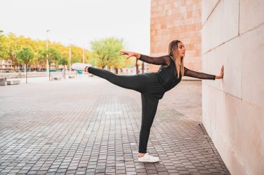 Siyah taytlı, beyaz spor ayakkabılı esnek bir kadın asfalt yolda dikiliyor ve başka tarafa bakıyor.