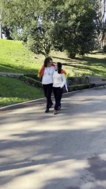 mother walking with her daughter carrying the lgtbi flag and putting it on her daughters shoulders. pride day