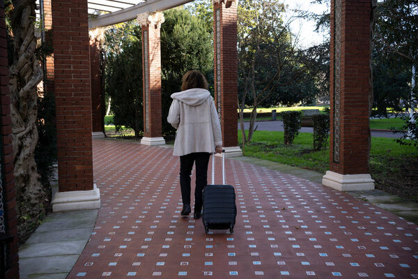 adult woman walking turning her back carrying a suitcase to go on vacation. vacation concept