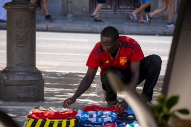 Granada, Granada, İspanya - 05 Ağustos 2023: Genç siyahi adamın yatay fotoğrafı Plaza Nueva 'da sokak satışı için futbol takımı gömleklerini hazırlıyor