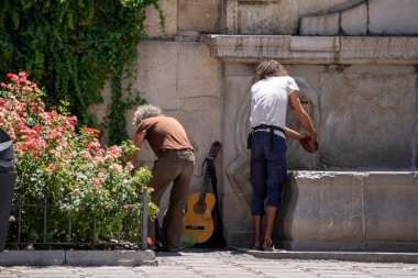 Granada, Granada, İspanya - 05 Ağustos 2023: Sokak müzisyenleri sokakta sadaka dilenmeye başlamadan önce Pilar del Toro çeşmesinde bulaşıkları yıkıyorlar