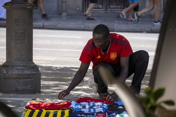 Granada, Granada, İspanya - 05 Ağustos 2023: Genç siyahi adamın yatay fotoğrafı Plaza Nueva 'da sokak satışı için futbol takımı gömleklerini hazırlıyor