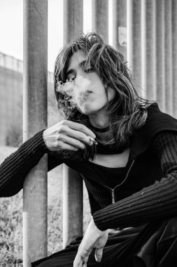 Ağzından duman üflerken elinde puro tutan genç adamın orta boy fotoğrafı. siyah beyaz fotoğraf. Dünya tütün günü konsepti