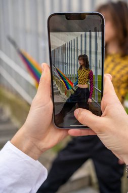 Kadın eli akıllı telefon tutuyor ve gururlu bir şemsiyeyle genç bir adamın fotoğrafını çekiyor. gurur günü konsepti